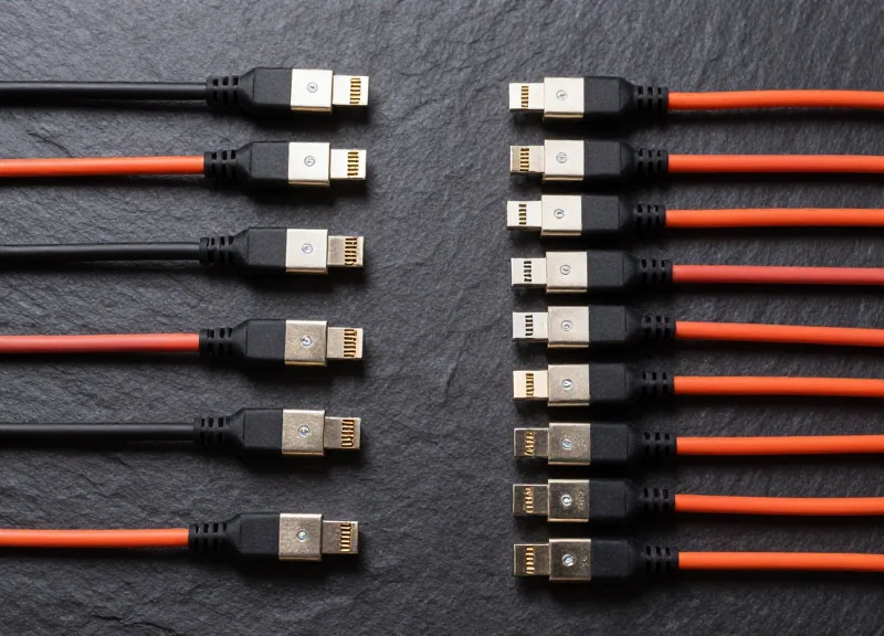 A professional flat lay arrangement of various high-speed DAC and AOC cables in different custom lengths, showing metallic SFP and QSFP connectors on a dark technical surface.